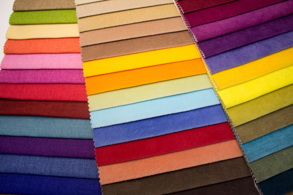 A person holding several kinds of t-shirt fabric swatches over a tabletop with natural lighting.