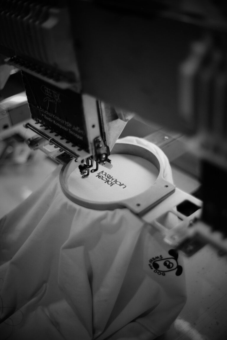 A person sketching apparel logo concepts on paper next to blank t-shirts and colored fabric swatches.